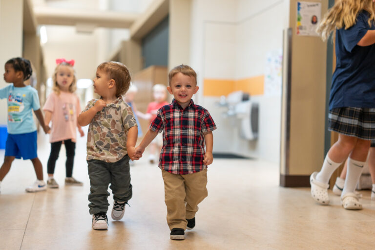 Young students hold hands as they walk down the hallway in pairs