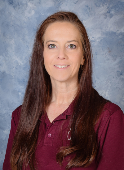 Portrait of Coach Kathy with long brown hair, smiling against a blue background.