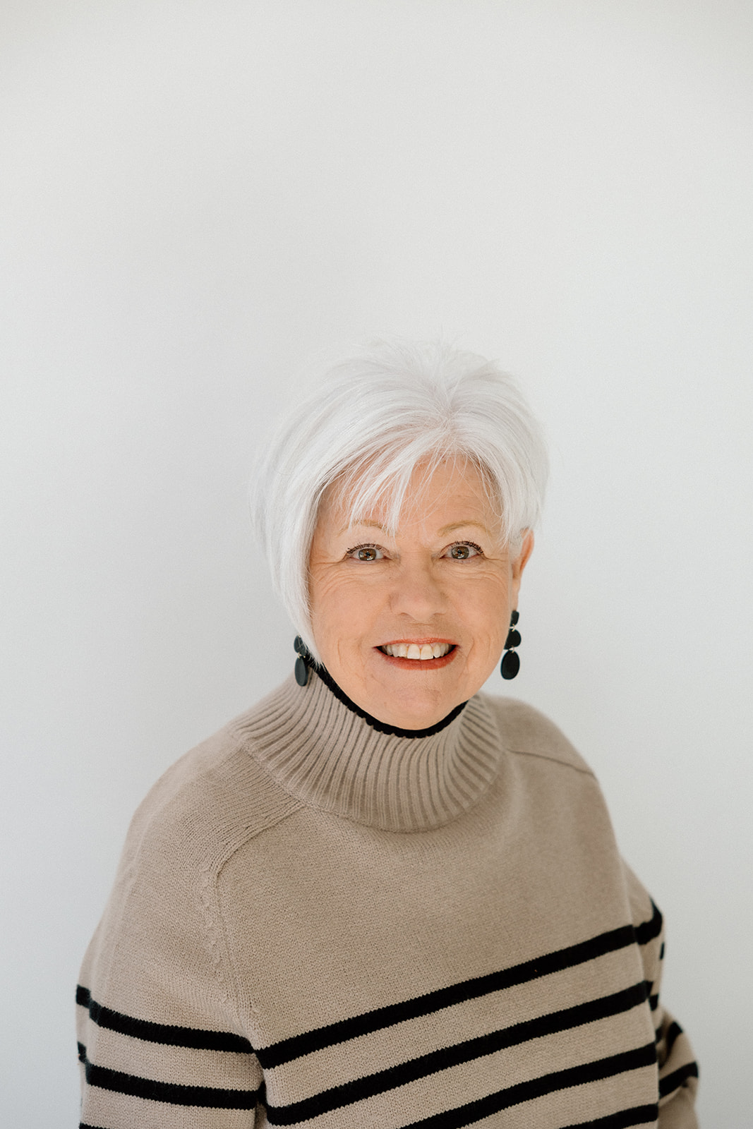Mature woman with white hair wearing a striped turtleneck sweater and earrings. Leadership & Staff.