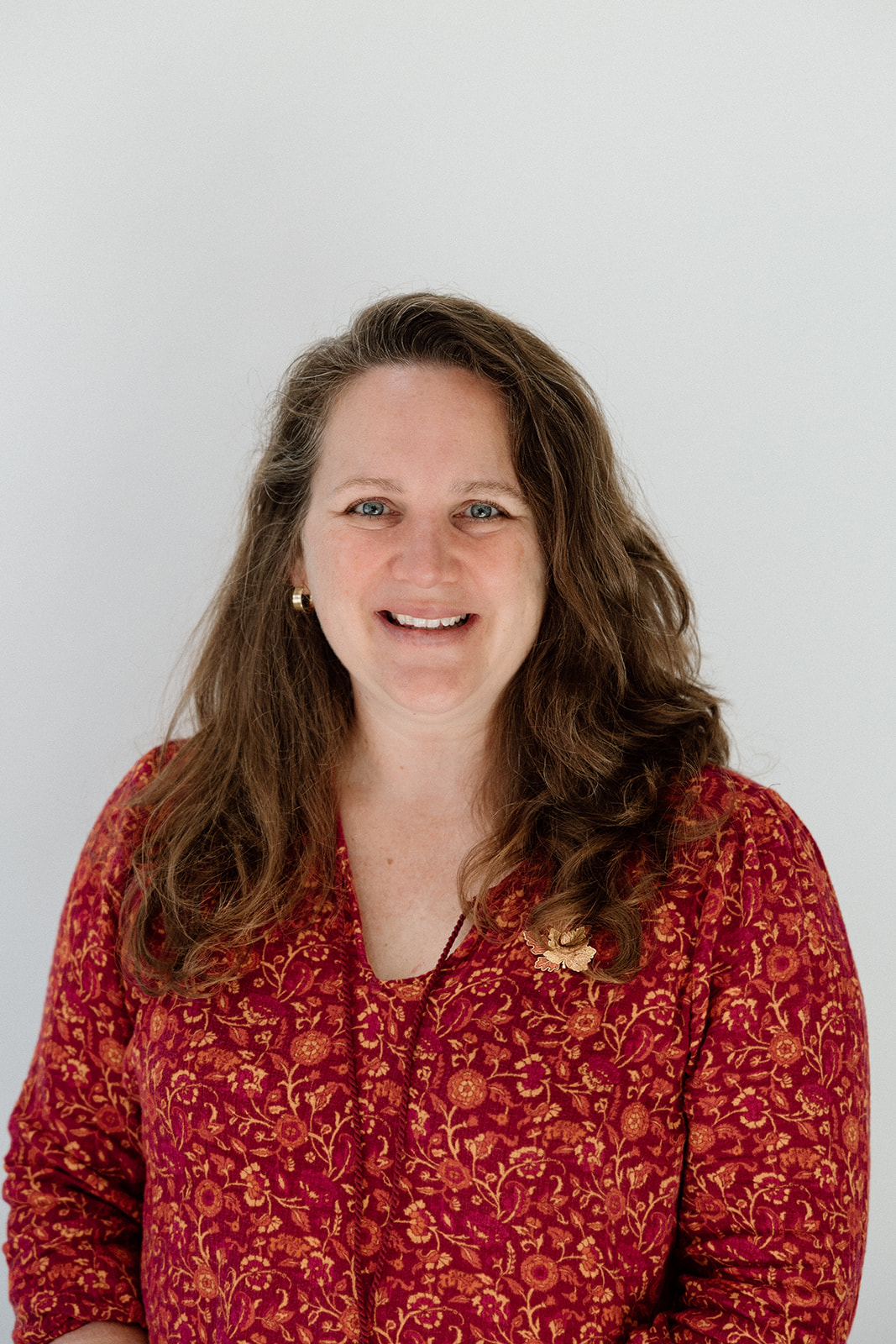 Woman in red floral blouse smiles warmly at the camera.