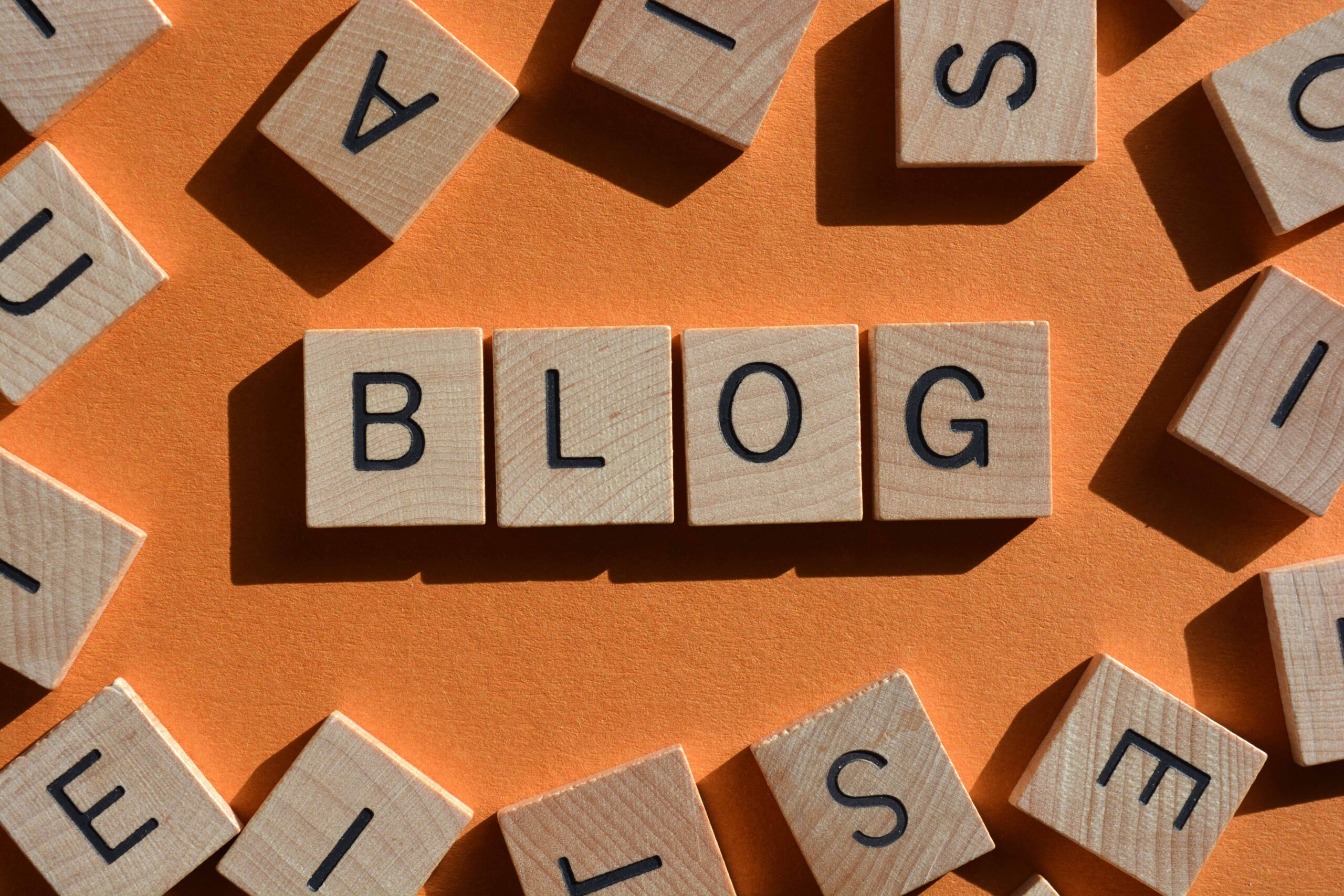Wooden blocks spelling "BLOG" surrounded by scattered letters on orange background.