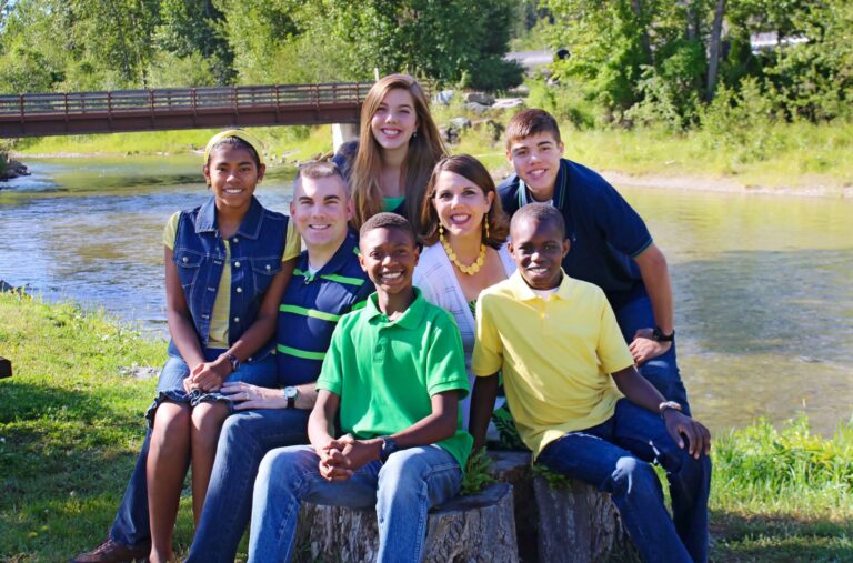 Christi White and family smiling by a river with a bridge in the background.