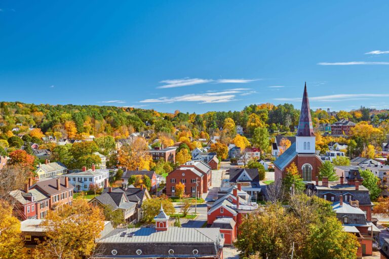 Autumn aerial view of a charming New England town with colorful foliage and a prominent church steeple.