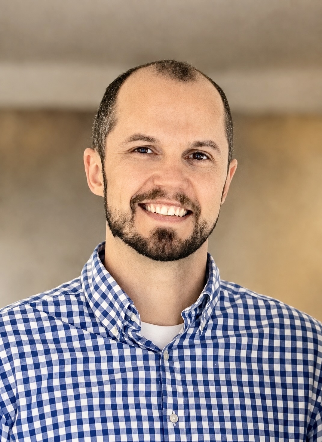 Caden Fouts, a smiling man with a beard wearing a blue gingham shirt.