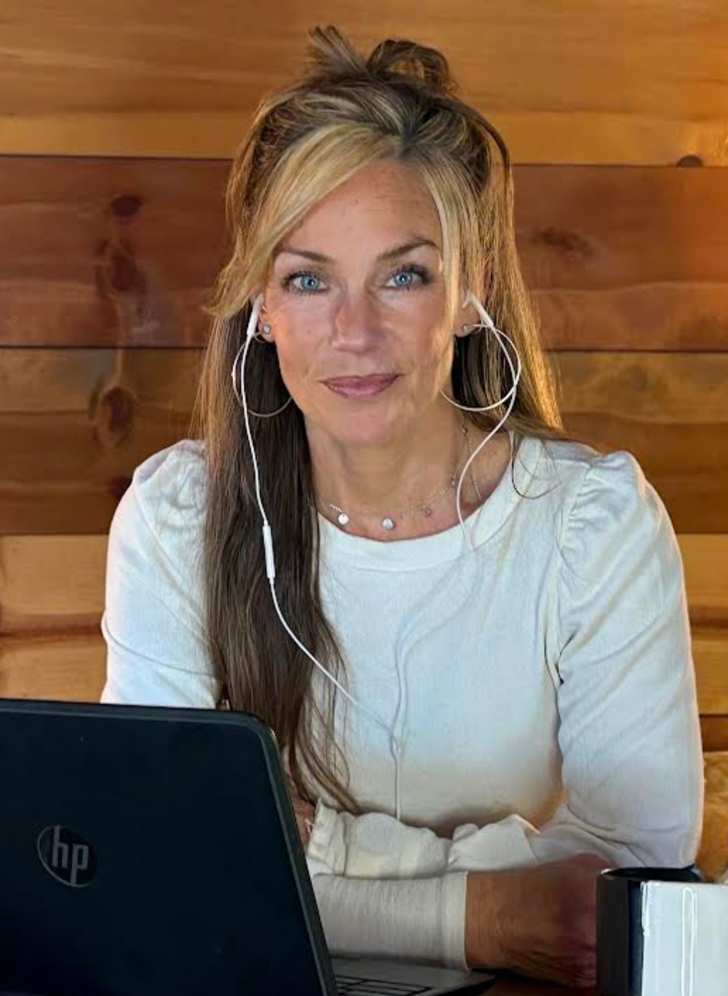 Heather Wilkinson, a blonde woman with blue eyes, wearing a white shirt and earbuds, works on a laptop.