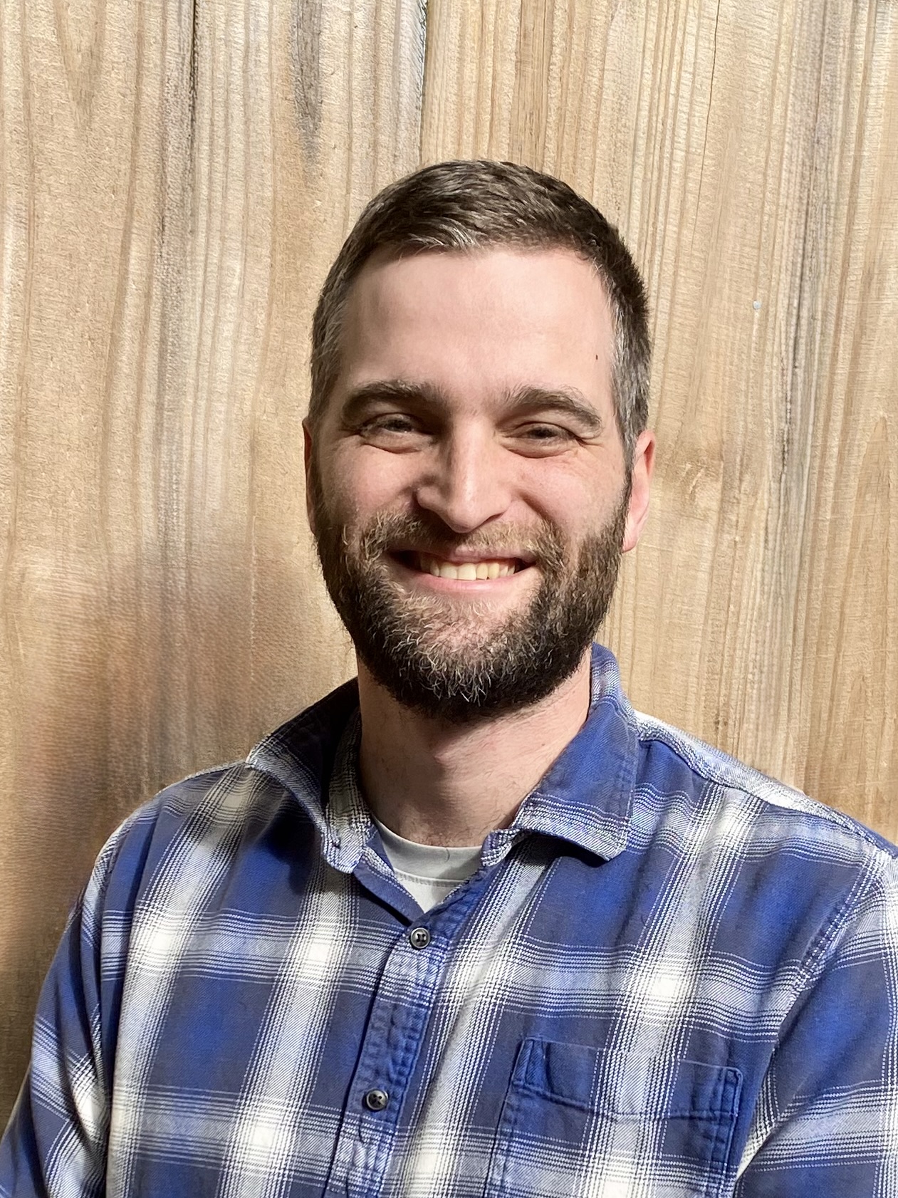 Jonathan Engle a man with a beard, smiles in a blue plaid shirt.