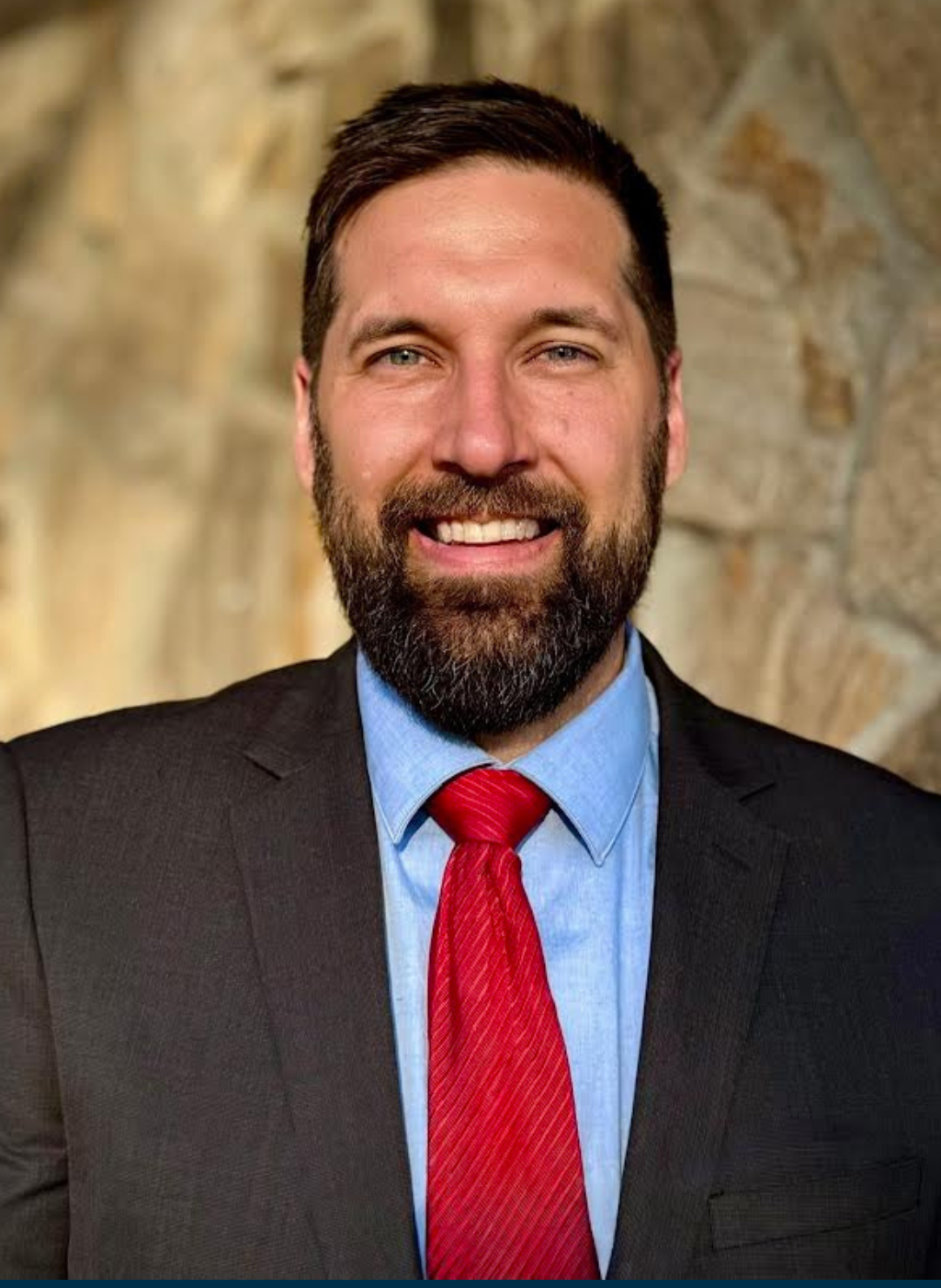 Luke Stockdale, a smiling man in a suit and red tie.